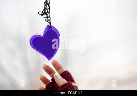 Femme dans les mains des mitaines pour atteindre le purple heart against a white background bokeh Banque D'Images