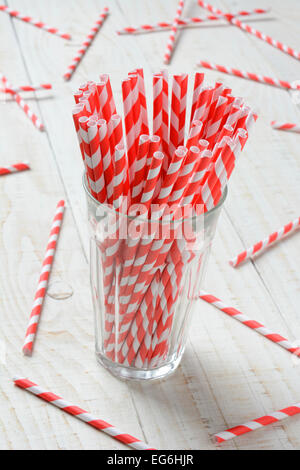 Libre d'un verre rempli de rouge et blanc à rayures pailles. Plus de papier paillettes sont épars sur le bois blanc rustique t Banque D'Images