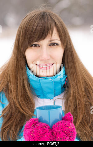 Smiling pretty girl holding tasse de thé chaud à l'extérieur d'hiver. Jeune femme aux longs cheveux bruns à la caméra directement dans Banque D'Images