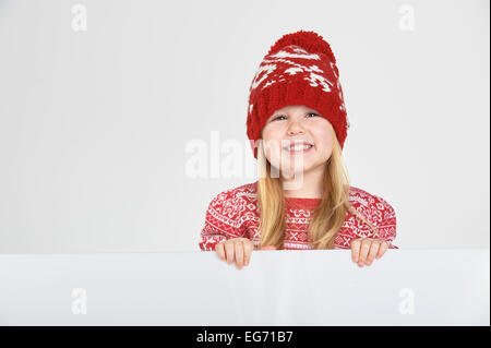 Smiling belle fille blonde dans un chapeau d'hiver rouge et blanc avec l'emplacement pour un texte ou une publicité Banque D'Images