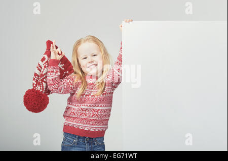 Smiling belle fille blonde dans un chapeau d'hiver rouge et blanc avec l'emplacement pour un texte ou une publicité Banque D'Images