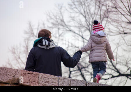 Père tenant sa fille par la main en marchant sur le bord d'un mur de pierre à l'extérieur Banque D'Images
