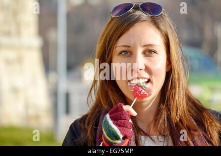 Girl biting forme de coeur bonbon sur une journée ensoleillée à l'extérieur Banque D'Images