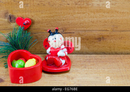 Petit coeur en céramique en forme de boîte remplie de bonbons colorés et d'une coccinelle ornement, sur une surface en bois Banque D'Images