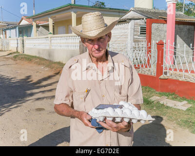 Un homme portant un chapeau de paille porte un grand carton d'oeufs le long d'une rue de terre à Viñales, Cuba. Banque D'Images