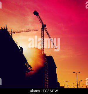 Silhouette de travailleur de la construction sur le toit de l'immeuble sur un site de construction dans le coucher du soleil. Banque D'Images