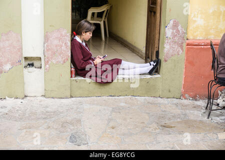 Belle mexicaine adolescente écolière avec cellphone & soda se trouve en face de la porte portant l'uniforme scolaire & bas blancs Banque D'Images