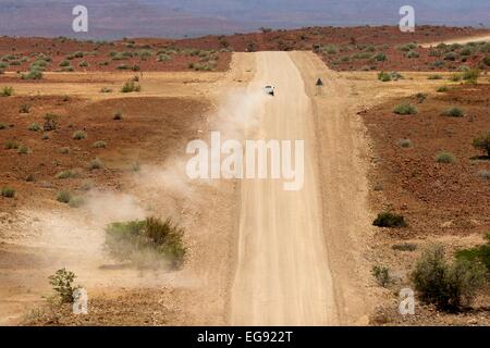 Un 4x4 blanc véhicule s'éloigne de la caméra sur une piste poussiéreuse à sec dans le nord de la Namibie, l'Afrique. Banque D'Images