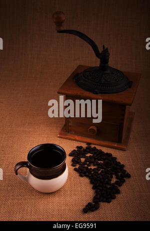 Tasse de café avec des grains de café et un vieux moulin sur l'arrière-plan, une image aux teintes chaleureuses avec vignette Banque D'Images