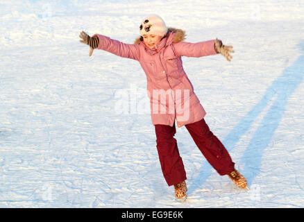 Jolie fille au chapeau et veste rose patinage sur glace un jour d'hiver ensoleillé Banque D'Images