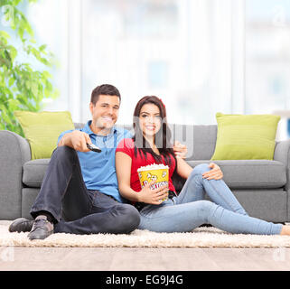 Jeune couple en regardant la télé assis sur le plancher à la maison avec un objectif de décentrement et Banque D'Images