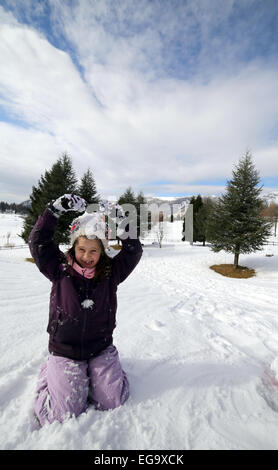 Jolie petite fille avec de la laine beret jouant sur la neige en hiver dans les montagnes Banque D'Images