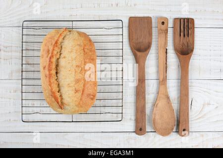 High angle shot d'une miche de pain frais cuit sur une grille de refroidissement avec une cuillère en bois, spatule et fourchette. Format horizontal Banque D'Images