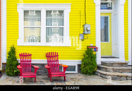 Lumineux, maison jaune avec deux chaises Adirondack rouge-orange à l'avant. Banque D'Images