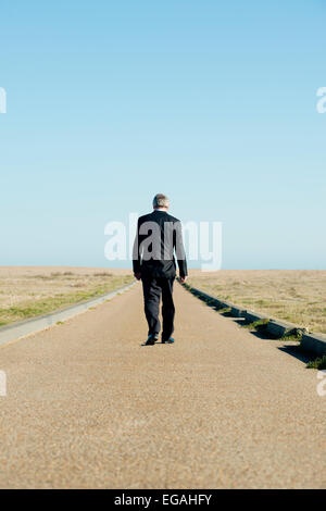 Businessman dans un costume sombre, qui s'éloignent d'appareil photo, le long d'un chemin sans fin à l'horizon. Banque D'Images