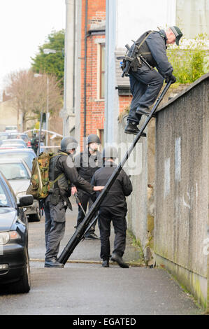 Les agents techniques de l'armée accompagnée par la police armée Rechercher Maisons et jardins d'explosifs à l'aide d'une échelle pour grimper aux murs et portes. Banque D'Images