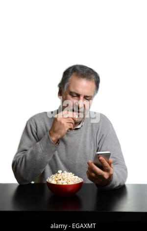 L'homme à l'aide de smart phone while eating popcorn at home Banque D'Images