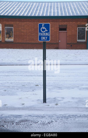 Seul signe de stationnement pour handicapés dans la neige parking en face de l'école élémentaire. Banque D'Images