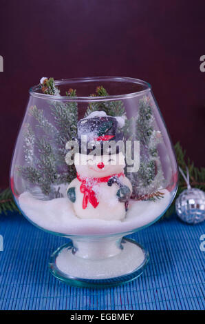 Bonhomme de jouet dans un vase en verre recouvert de neige sur un fond bleu Banque D'Images