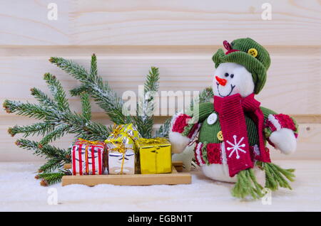 Bonhomme de jouet entre les sapins et présente sur une surface en bois enneigé Banque D'Images