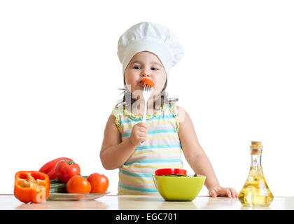 Kid girl dans cook hat manger des légumes Banque D'Images