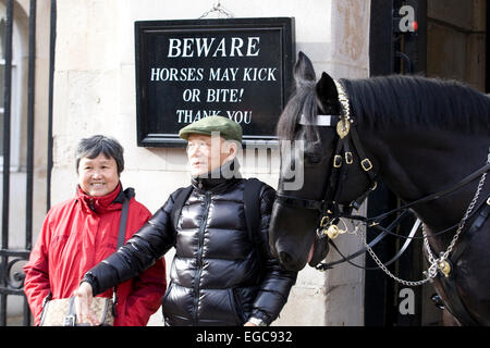 Les touristes asiatiques à Horseguards Parade debout sous un panneau disant 'Warning les chevaux peuvent rejoindre votre chambre ou morsure merci' avec l'essayer d'étouffer Banque D'Images