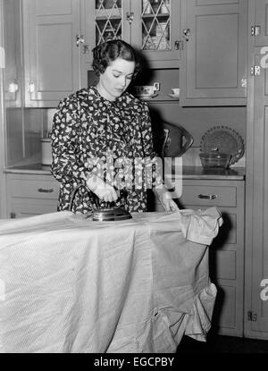 Années 1930 Années 1940 femme portant un tablier blouse imprimé l'article planche à repasser Fer à repasser électrique poussant Banque D'Images