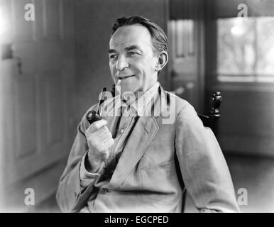 1940 MAN SMILING HOLDING FUMEURS PIPE PORTANT CHEMISE EN JEAN VESTE TRAVAIL SITTING IN CHAIR CARACTÈRE RURAL AGRICULTEUR Banque D'Images