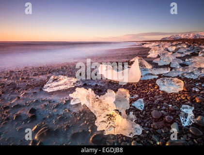 La glace brisée d'icebergs échoués sur la plage noire Jokulsarlon au lever du soleil avec une vitesse lente de l'eau laiteuse du sud est de l'Islande Jokulsarlon Banque D'Images