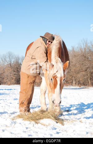 Man hugging un grand cheval de trait belge, emmitouflés dans des vêtements d'hiver sur une froide journée d'hiver amer Banque D'Images