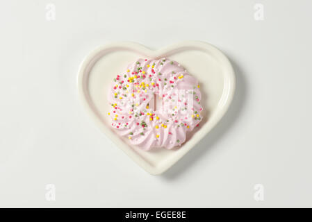 Couronne de meringue rose garni de biscuit sur la plaque en forme de coeur sprinkles Banque D'Images