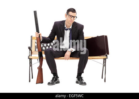 Upset businessman tenant un fusil assis sur un banc isolé sur fond blanc Banque D'Images