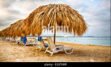 Chaises de salon sous le chaume umbellas sur le sable blanc d'un complexe en front de mer des Caraïbes. Banque D'Images