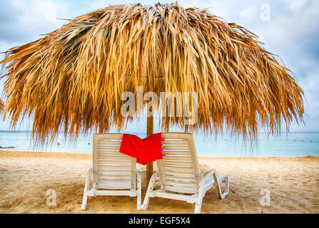 Chaises de salon sous le chaume umbellas sur le sable blanc d'un complexe en front de mer des Caraïbes. Banque D'Images