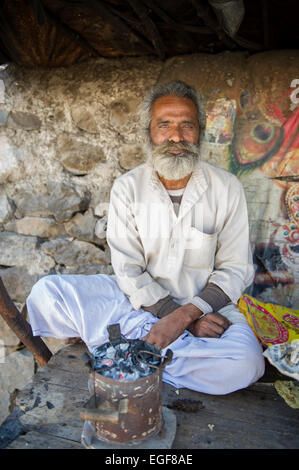 Un commerçant de rue locaux assis avec son poêle sous l'abri de son petit côté route par la canopée à Rishikesh, Inde, Uttarkahand Banque D'Images