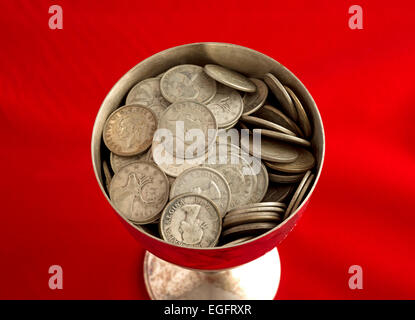 Ancien gobelet rempli de lingots d'argent canadien trimestre sur un tissu rouge de table. Banque D'Images