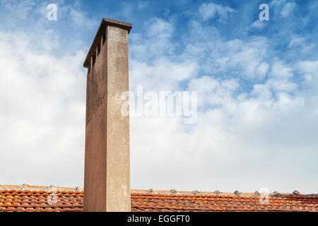 Haute cheminée sur toiture tuile rouge avec fond de ciel nuageux Banque D'Images