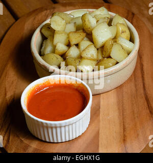 Tapas : patatas bravas. Dés de pommes de terre cuites avec de la sauce tomate épicée servi dans des bols en céramique sur une plaque de bois Banque D'Images