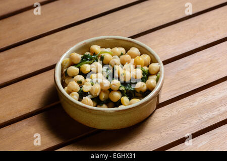 Des tapas. Les épinards et pois chiches cuits dans une sauce épicée, servi dans un bol en céramique marron sur une table en bois Banque D'Images