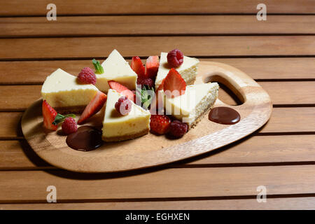 Le Dessert. Cheese cake à la framboise, fraise et chocolat sauce avec feuille de menthe sur une plaque de bois. Mur arrière-plan. Banque D'Images