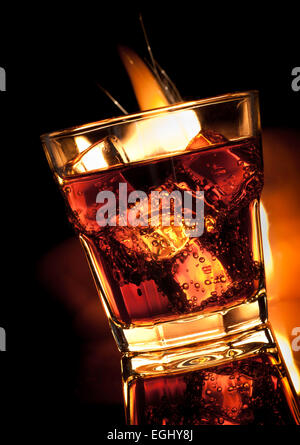 Cola avec du whisky dans le verre et le feu sur noir Banque D'Images