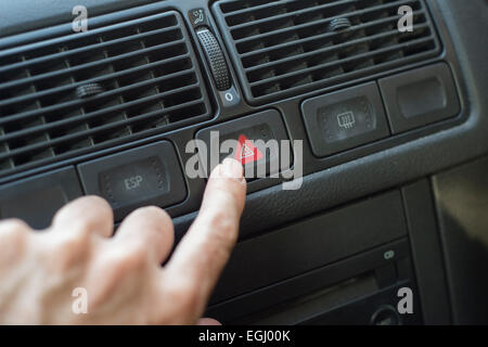 À propos de doigt pour pousser l'interrupteur de feux de détresse dans une voiture Banque D'Images