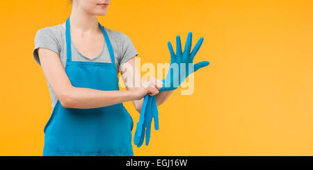 Femme de se préparer pour le nettoyage de printemps, de mettre des gants en caoutchouc sur bleu Banque D'Images