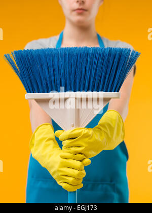 Close-up of cleaning woman holding blue balai en face d'elle, sur fond jaune Banque D'Images