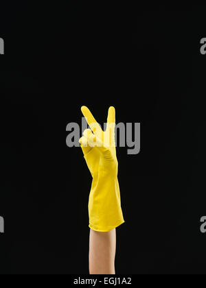 Jusqu'à la main avec des gants jaune montrant la victoire, sur fond noir Banque D'Images