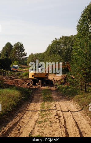 La construction de routes.Le constructeur sur l'excavatrice creuse le sable pour le pont - un tuyau à travers un flux. Banque D'Images