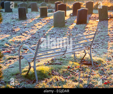 Frost couverts métal et pierres tombales siège dans un village cimetière dans le Herefordshire, au Royaume-Uni, à l'aube d'un matin d'hiver gelé. Banque D'Images