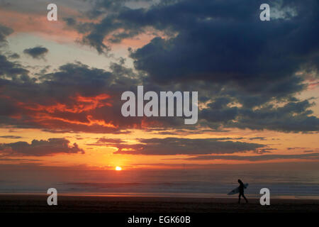 Surfer sur l'océan plage au coucher du soleil avec des nuages sombres Banque D'Images