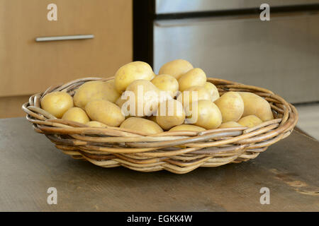 Les pommes de terre jaunes frais dans le panier tissé sur la table de cuisine Banque D'Images