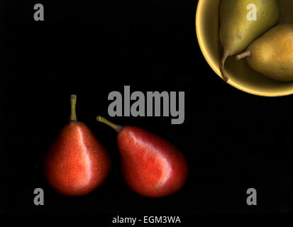 Fruits rouges et jaunes, les poires dans un bol de cuisine isolé sur un fond noir Banque D'Images